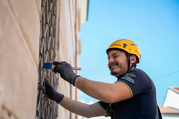 Hombre con casco amarillo sonríe mientras realiza el revoco de paredes con una brocha azul.