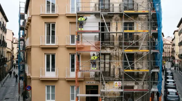 Trabajadores en andamios rehabilitan fachadas de edificios en una calle urbana.