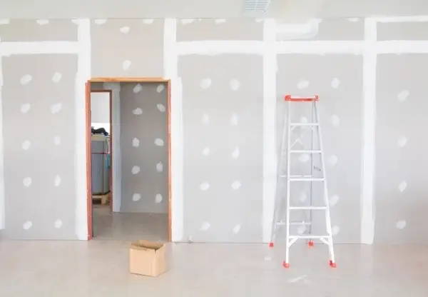 Habitación en construcción con paredes de enfoscado de yeso, una escalera y una caja de cartón.